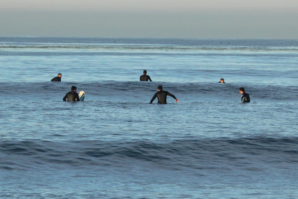 group of men in wetsuits sitting on their surfboards in the ocean waiting at the break for the next set of waves to come in