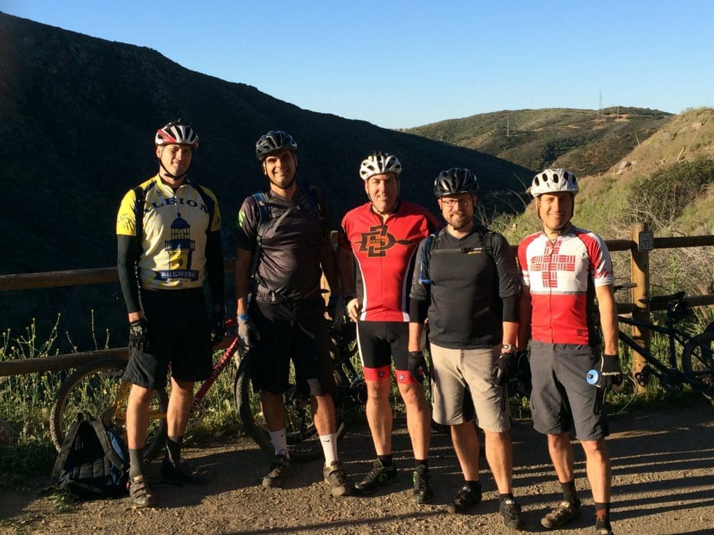 group of men in mountain biking gear posing in front of hill range